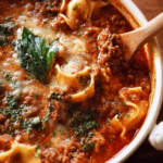 Close-up of hearty one pot lasagna soup with ground beef, lasagna noodles, melted cheese, and fresh basil, served hot in a white bowl with a wooden spoon.