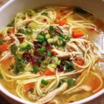 Bowl of aromatic ginger garlic chicken noodle soup with fresh herbs.