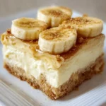 Delicious banana pudding cheesecake squares on a plate, topped with whipped cream.